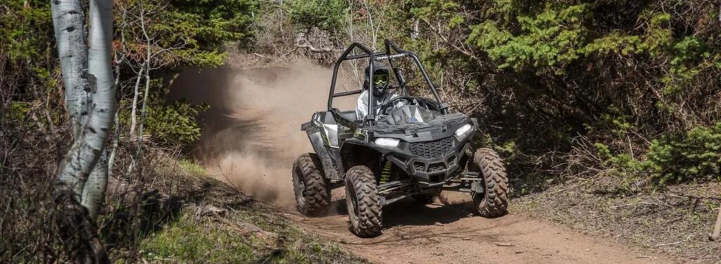 ATV driving on a dirt path in a dense forest, kicking up dust while navigating the rugged terrain.